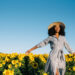 Happy young woman walking in a sunflower field.